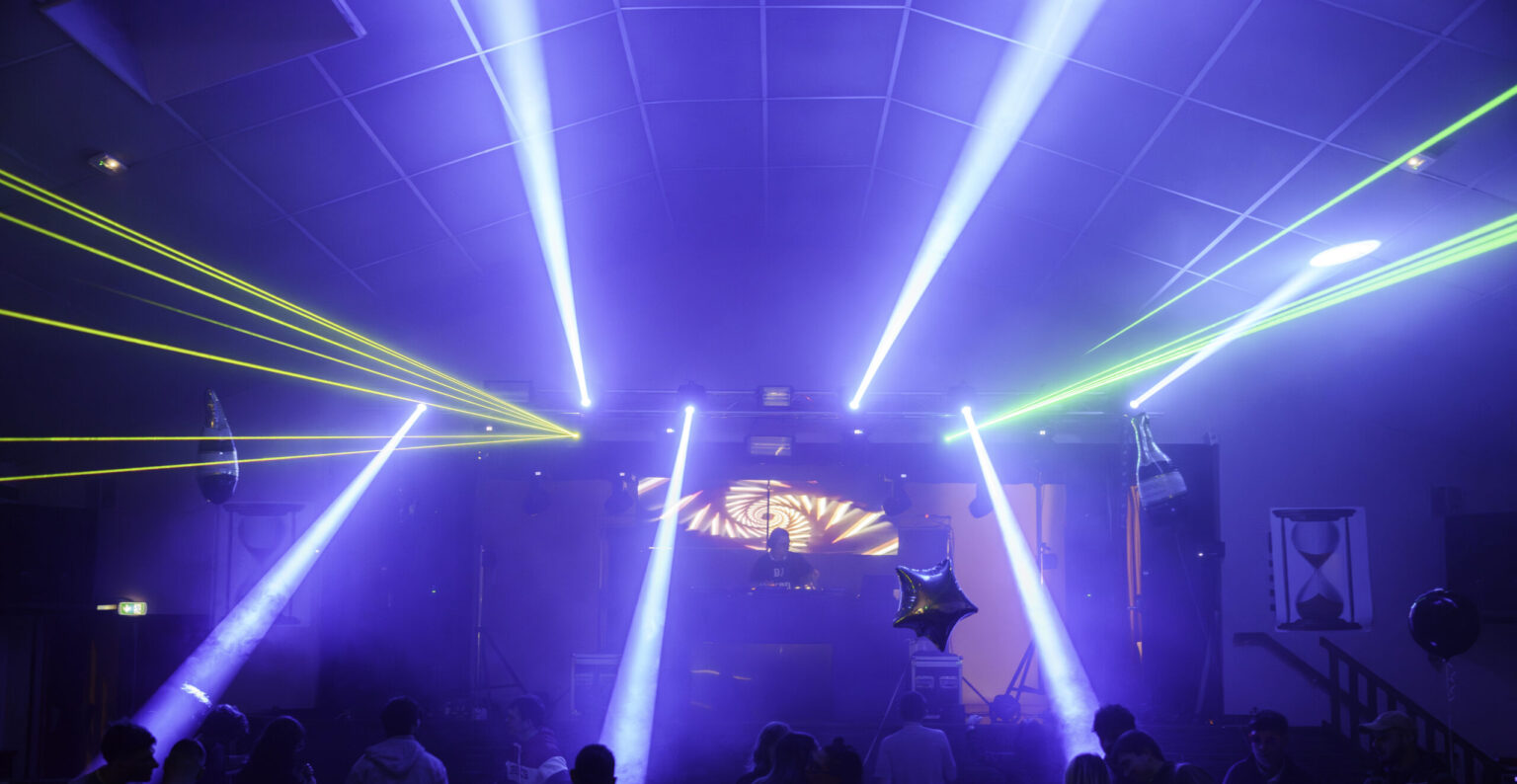 Salle plongée dans l'obscurité, faisceaux laser verts et bleus au-dessus du public, lors de la première édition du festival Head of Time